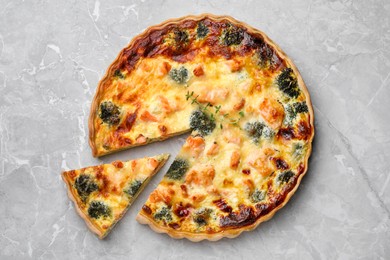 Photo of Delicious homemade quiche with salmon and broccoli on light gray marble table, flat lay