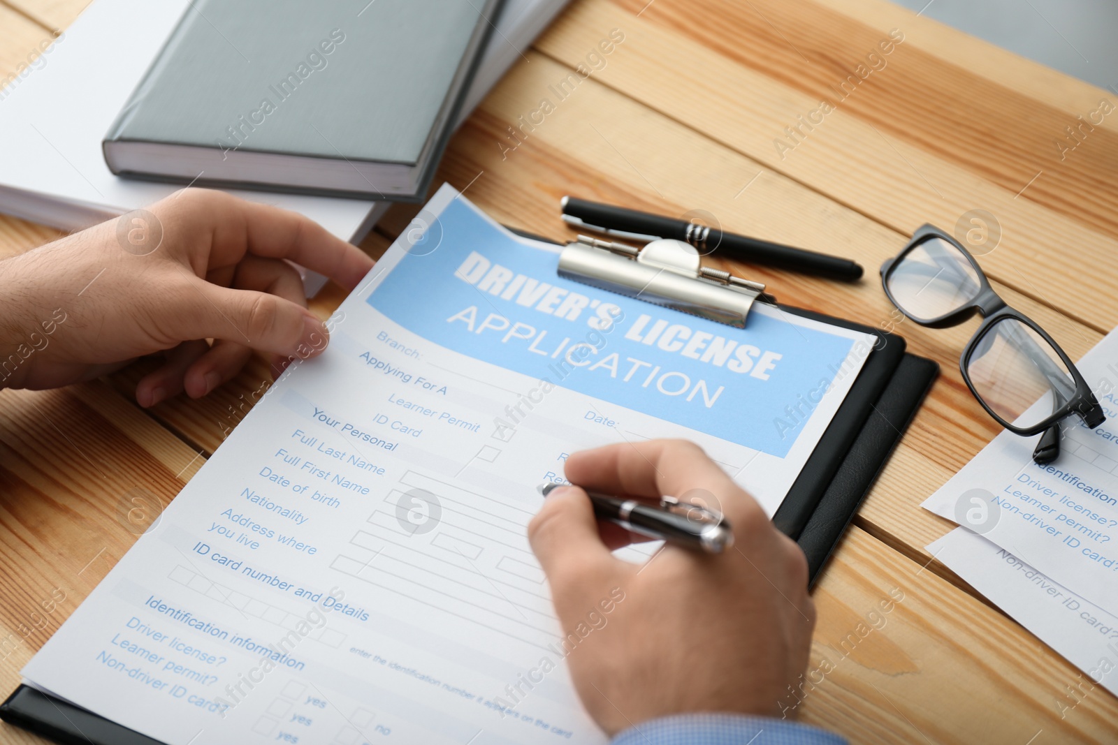 Photo of Man filling in driver's license application form at wooden table, closeup