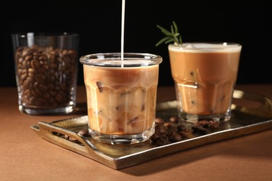 Photo of Pouring milk into glass with refreshing iced coffee at brown table