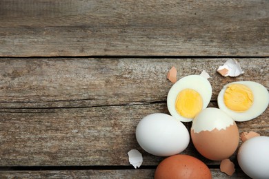 Photo of Hard boiled eggs and pieces of shell on wooden table, flat lay. Space for text