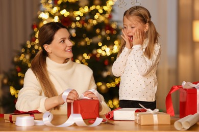 Photo of Christmas presents wrapping. Mother and her emotional daughter decorating gift box with ribbon at home