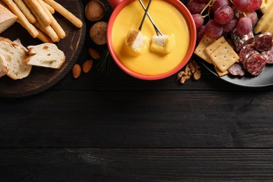 Photo of Pot of tasty cheese fondue and snacks on black wooden table, flat lay. Space for text