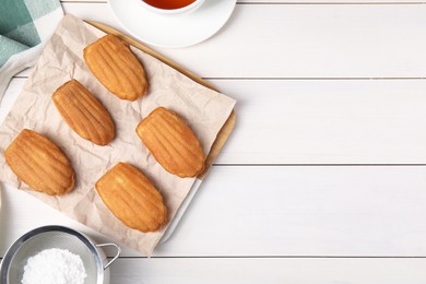 Photo of Tasty madeleine cookies, tea and powdered sugar on white wooden table, flat lay. Space for text