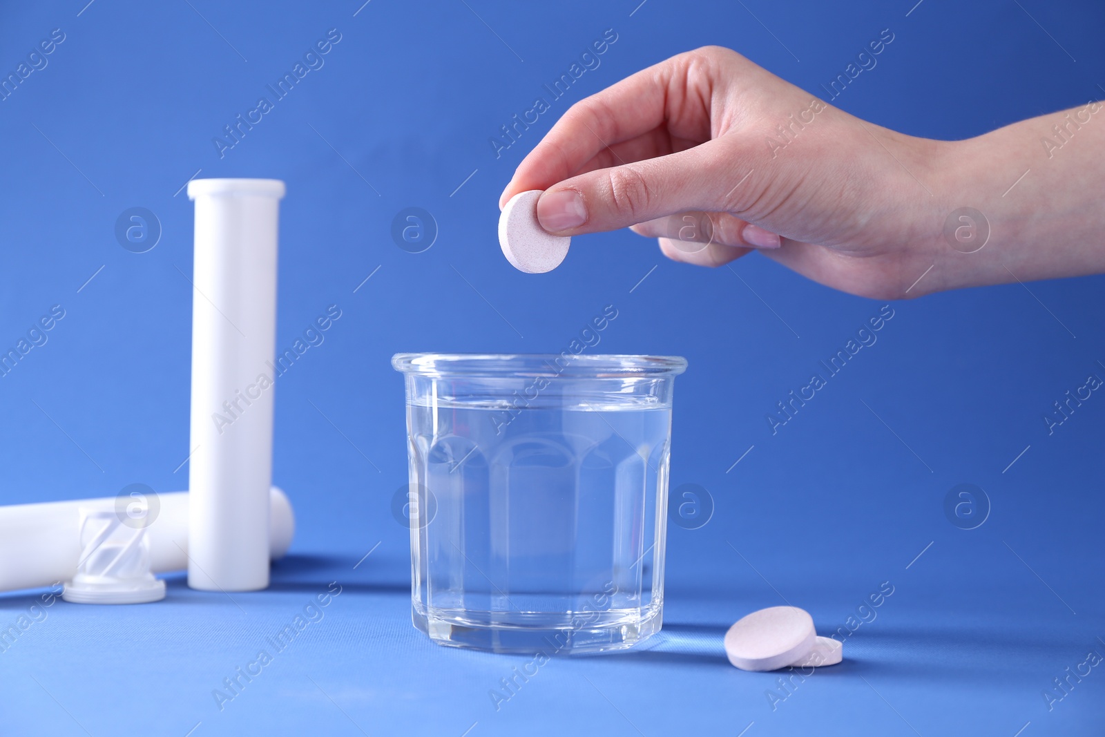 Photo of Woman putting effervescent pill into glass of water on blue background, closeup