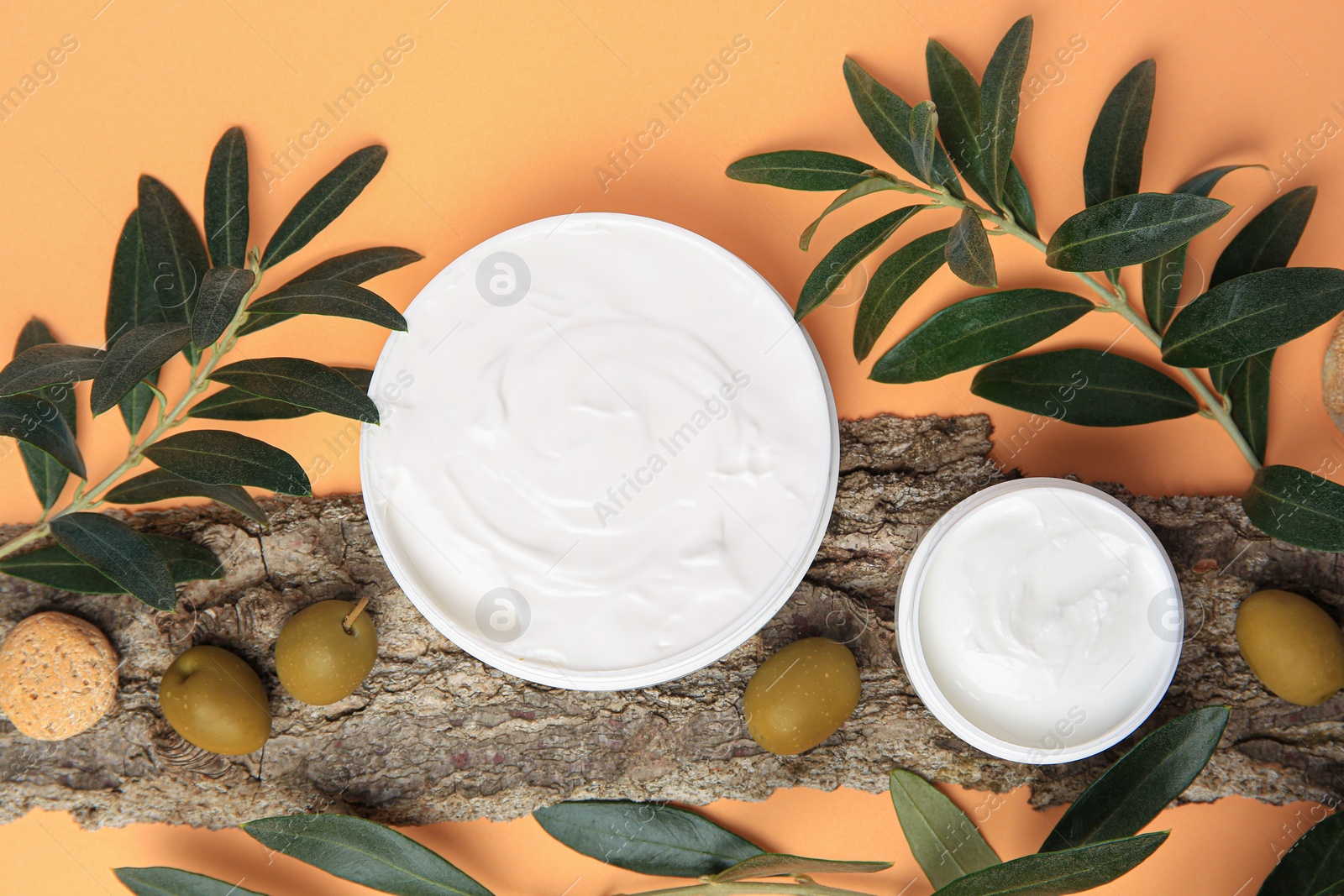 Photo of Flat lay composition with jars of cream and olives on pale orange background