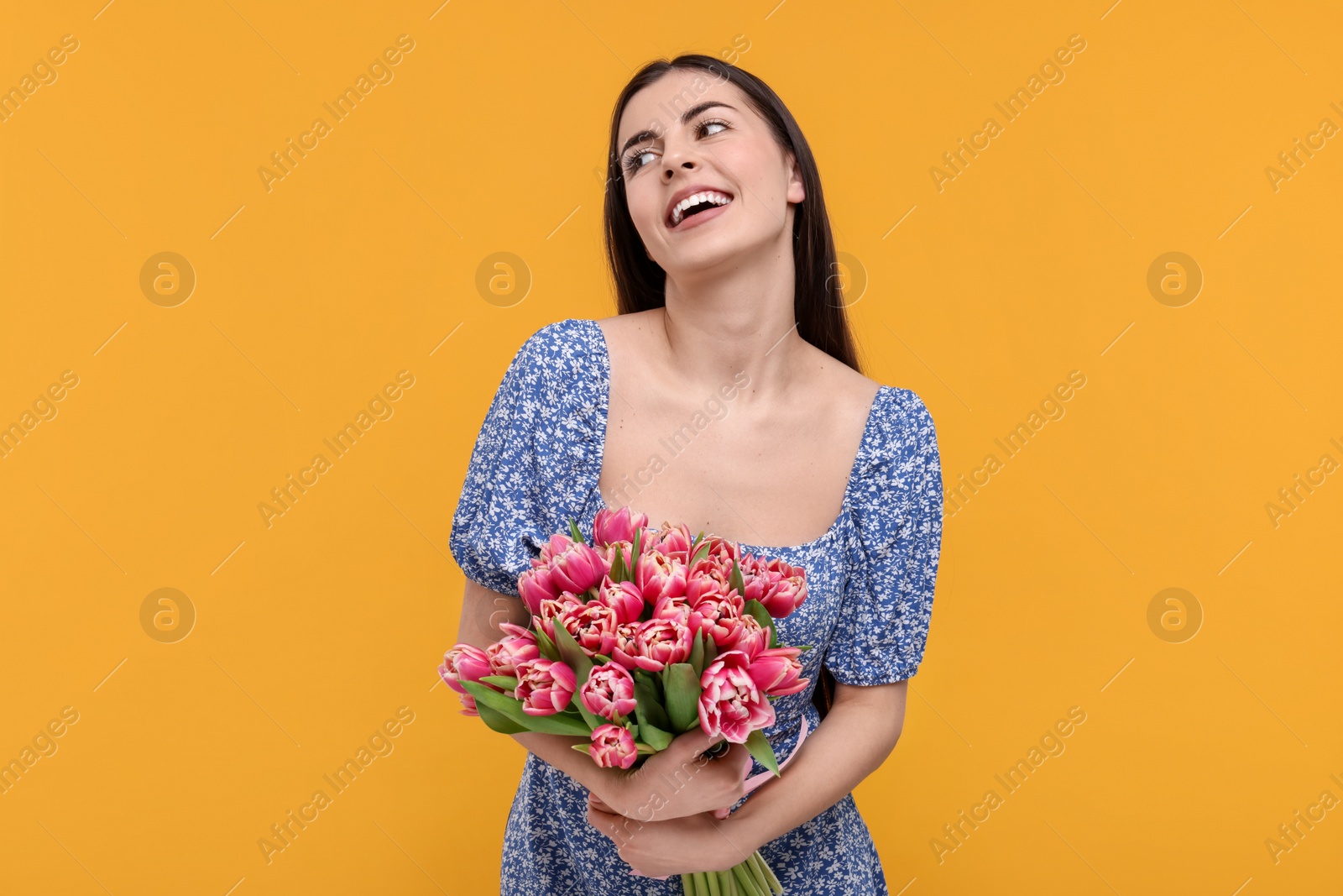 Photo of Happy young woman with beautiful bouquet on orange background