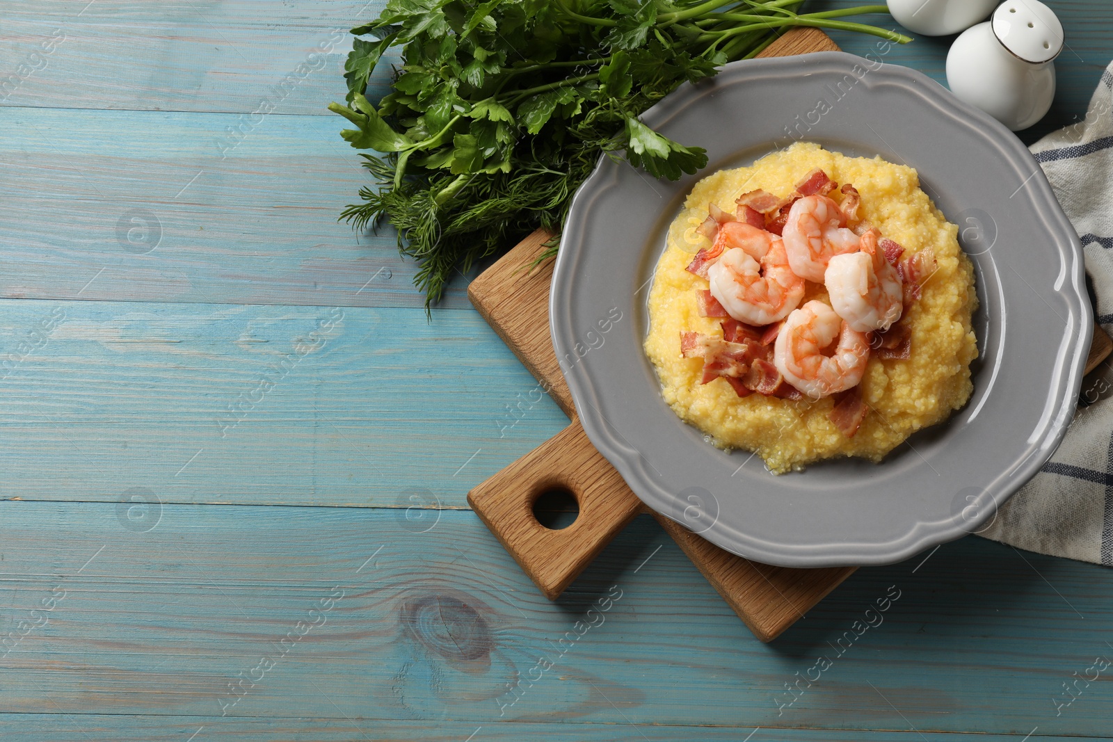 Photo of Plate with fresh tasty shrimps, bacon and grits on light blue wooden table, flat lay. Space for text