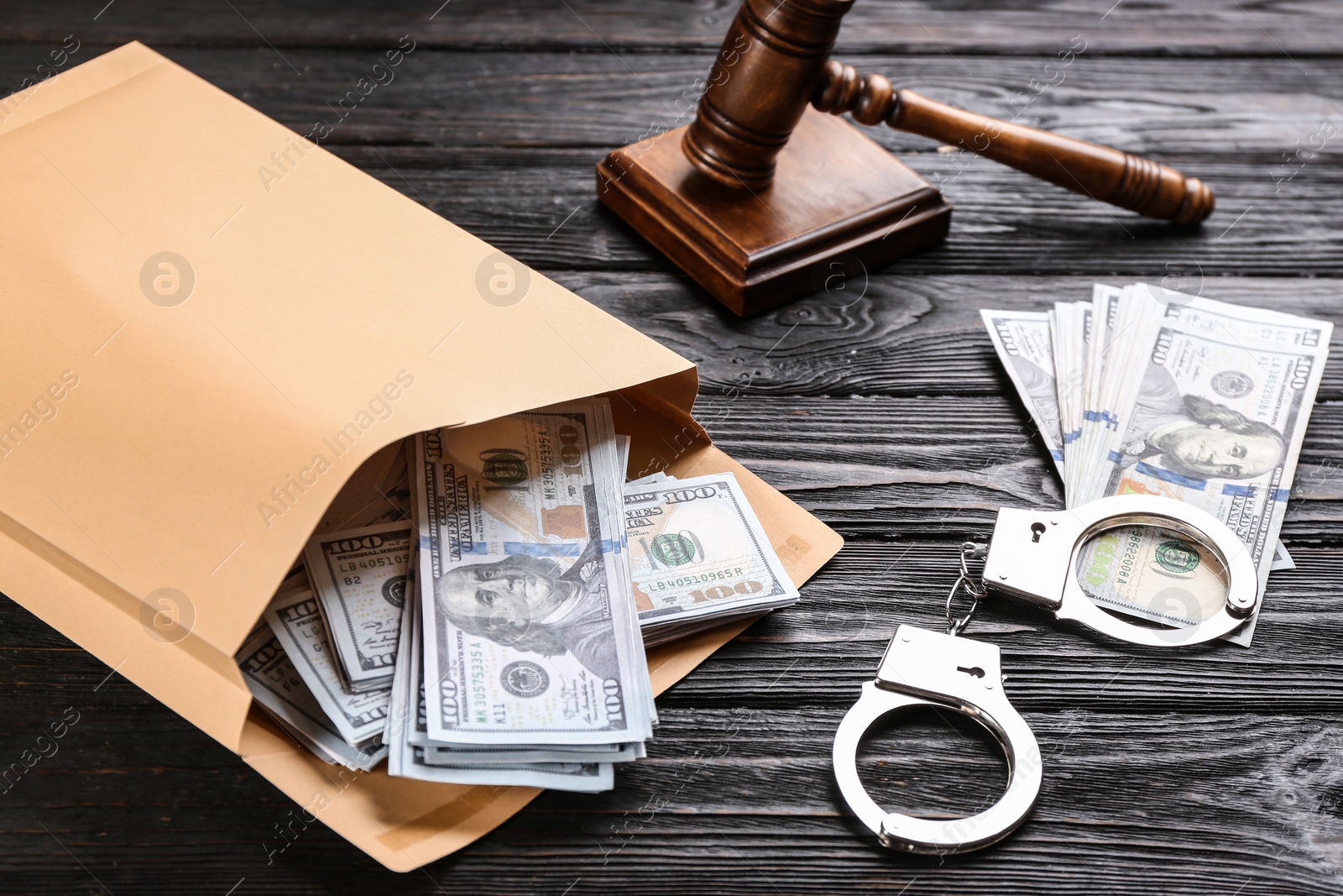 Photo of Envelope with dollar bills and handcuffs on black wooden table. Bribe concept