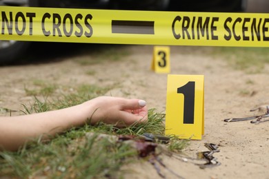 Photo of Crime scene with dead woman's body, marker, bloody knife and yellow tape outdoors, closeup