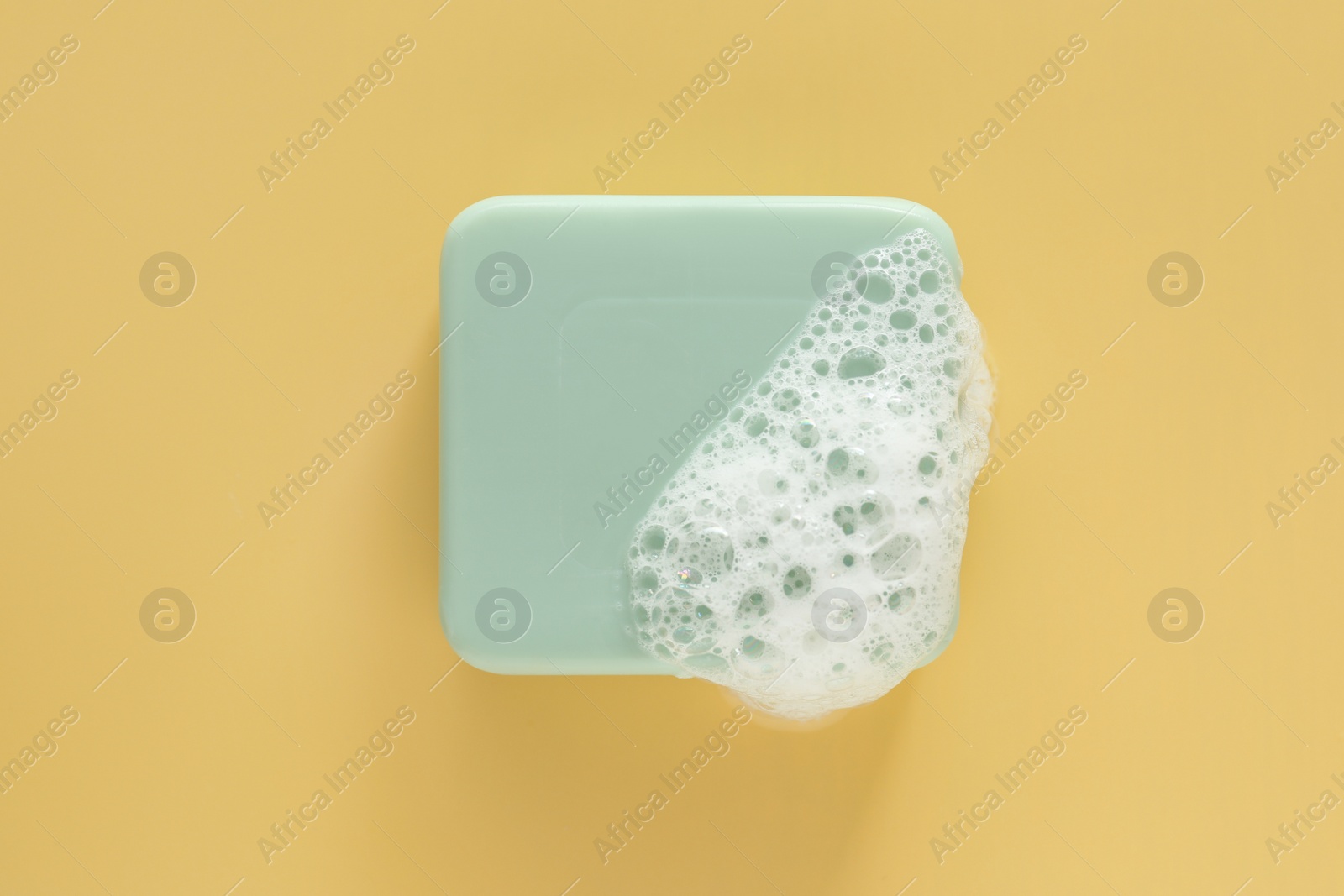Photo of Soap bar with fluffy foam on yellow background, top view