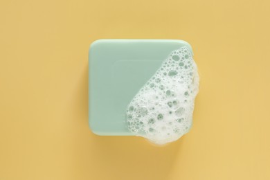 Soap bar with fluffy foam on yellow background, top view