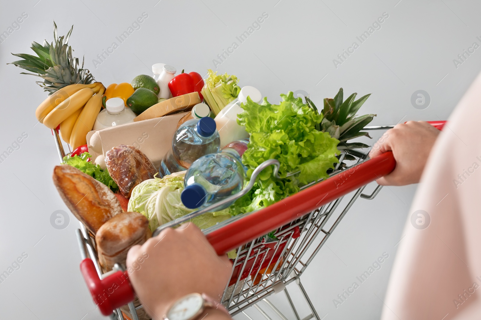 Photo of Woman with shopping cart full of groceries on grey background, closeup