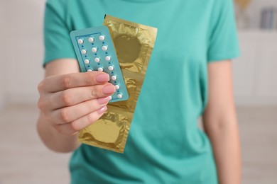 Photo of Woman holding condoms and contraceptive pills on blurred background, closeup. Choosing birth control method