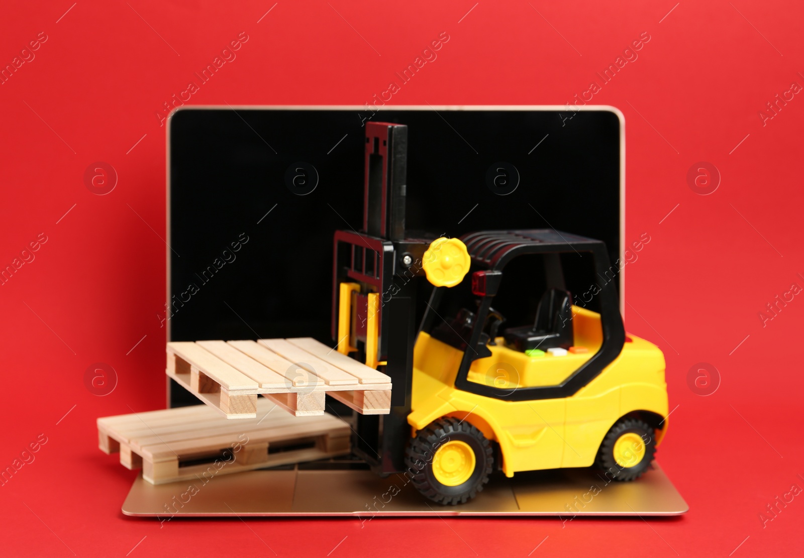 Photo of Laptop, toy forklift and wooden pallets on red background