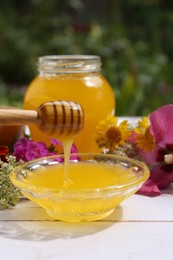 Photo of Delicious honey flowing down from dipper into bowl on white wooden table in garden