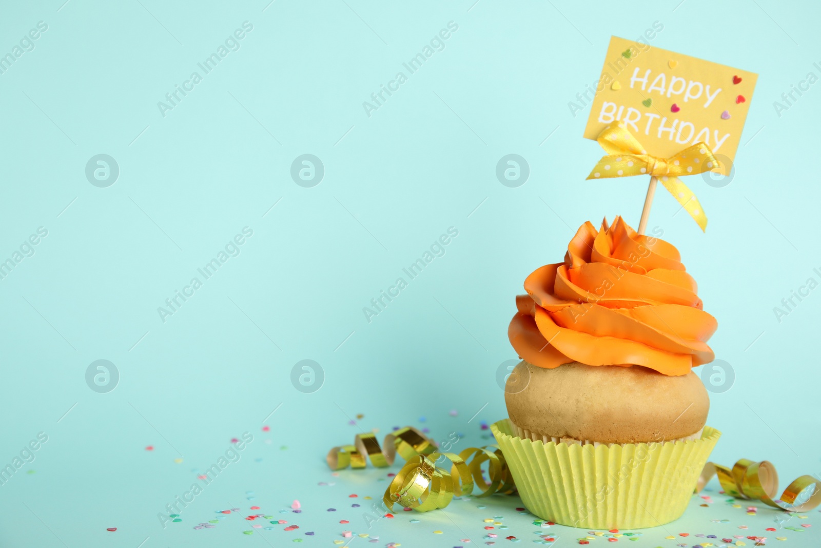 Photo of Beautiful birthday cupcake, streamers and confetti on light blue background. Space for text