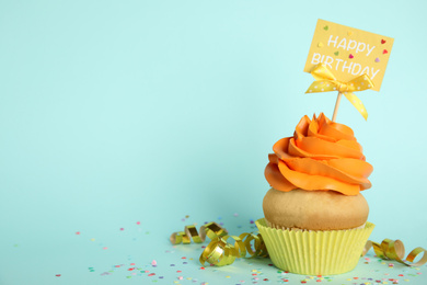 Photo of Beautiful birthday cupcake, streamers and confetti on light blue background. Space for text