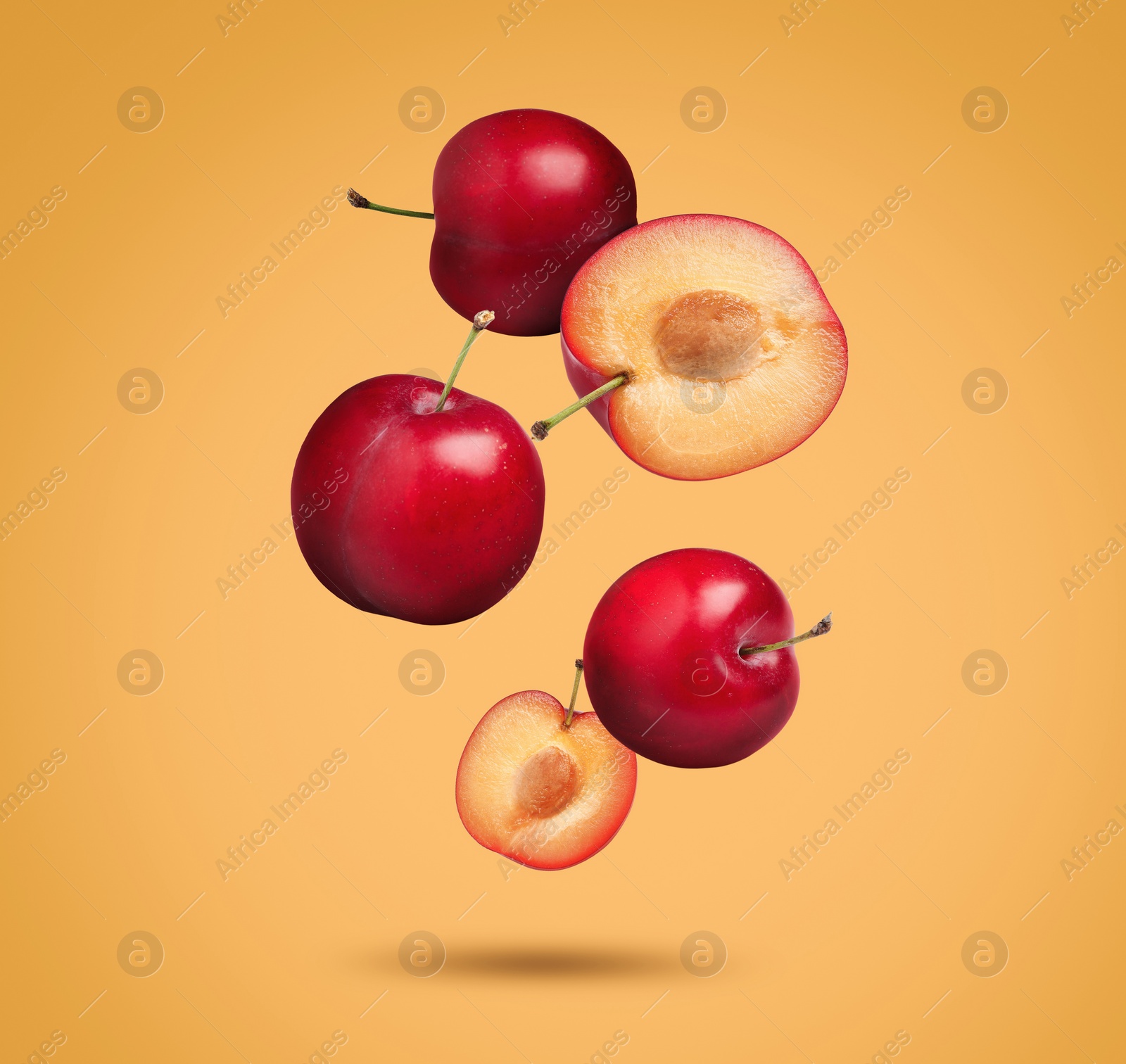 Image of Many fresh cherry plums falling on orange background