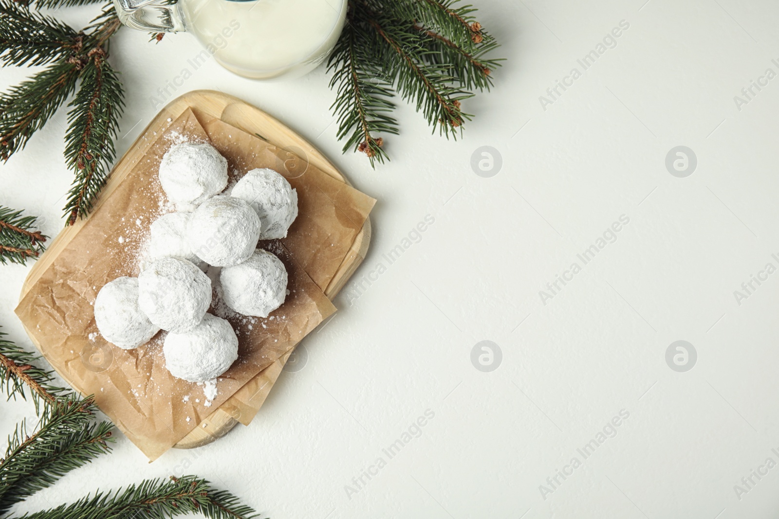 Photo of Christmas snowball cookies and fir branches on white table, flat lay. Space for text