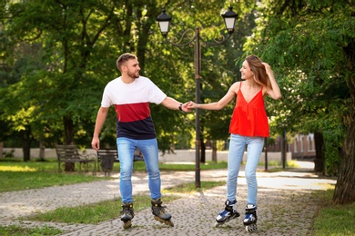 Photo of Young happy couple roller skating in summer park