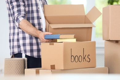Photo of Man putting books into box indoors, closeup. Moving day