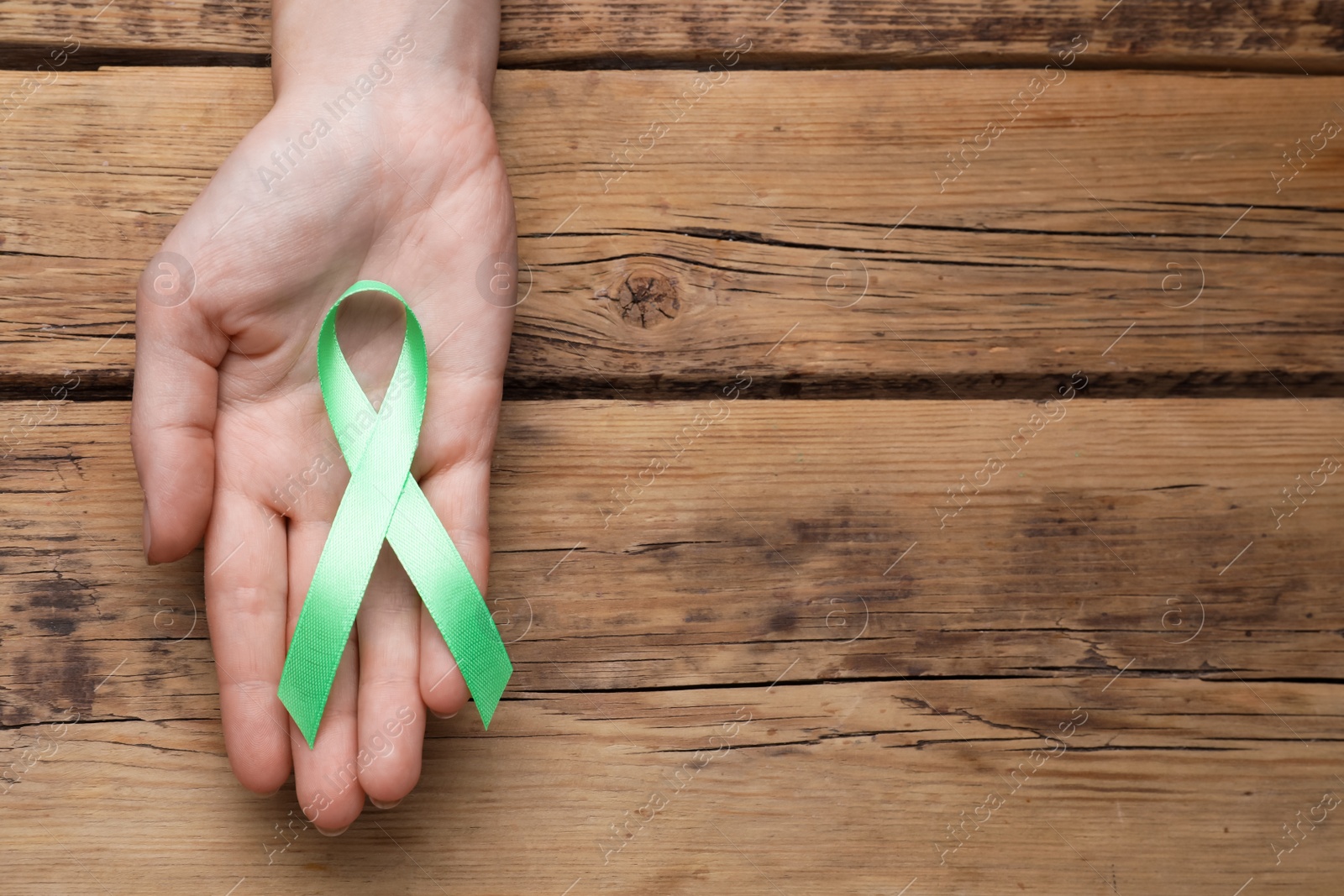 Photo of World Mental Health Day. Woman holding green ribbon on wooden background, top view with space for text