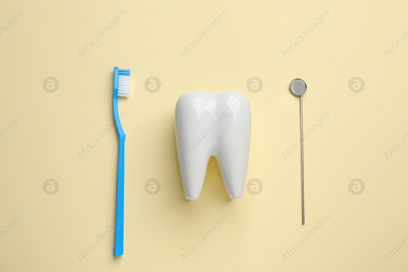 Photo of Tooth shaped holder, brush and dentist's mirror on pale yellow background, flat lay