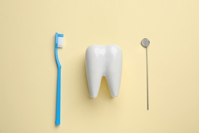 Photo of Tooth shaped holder, brush and dentist's mirror on pale yellow background, flat lay