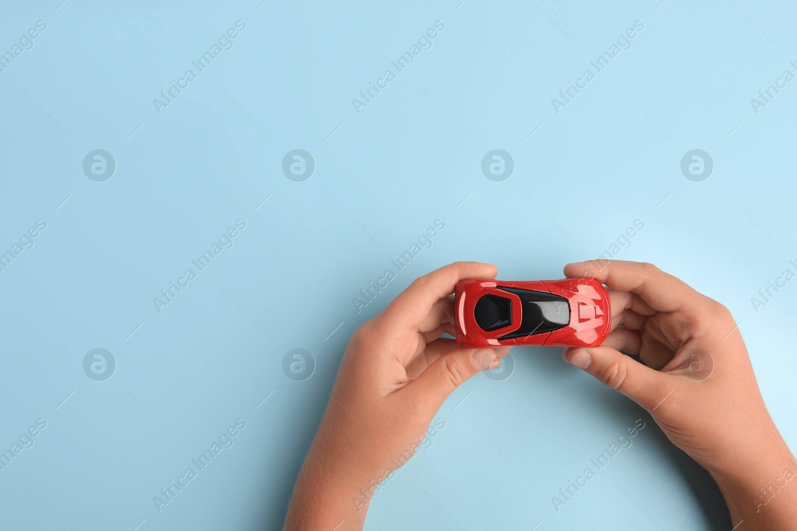 Photo of Child holding toy car on light blue background, top view. Space for text