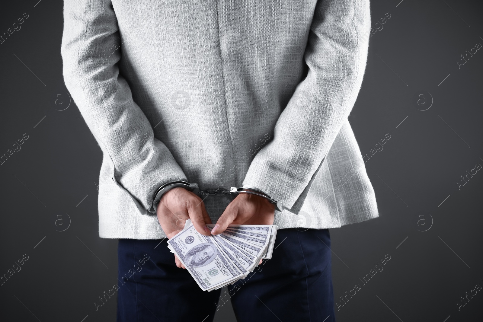 Photo of Man in handcuffs holding bribe money on dark background, closeup