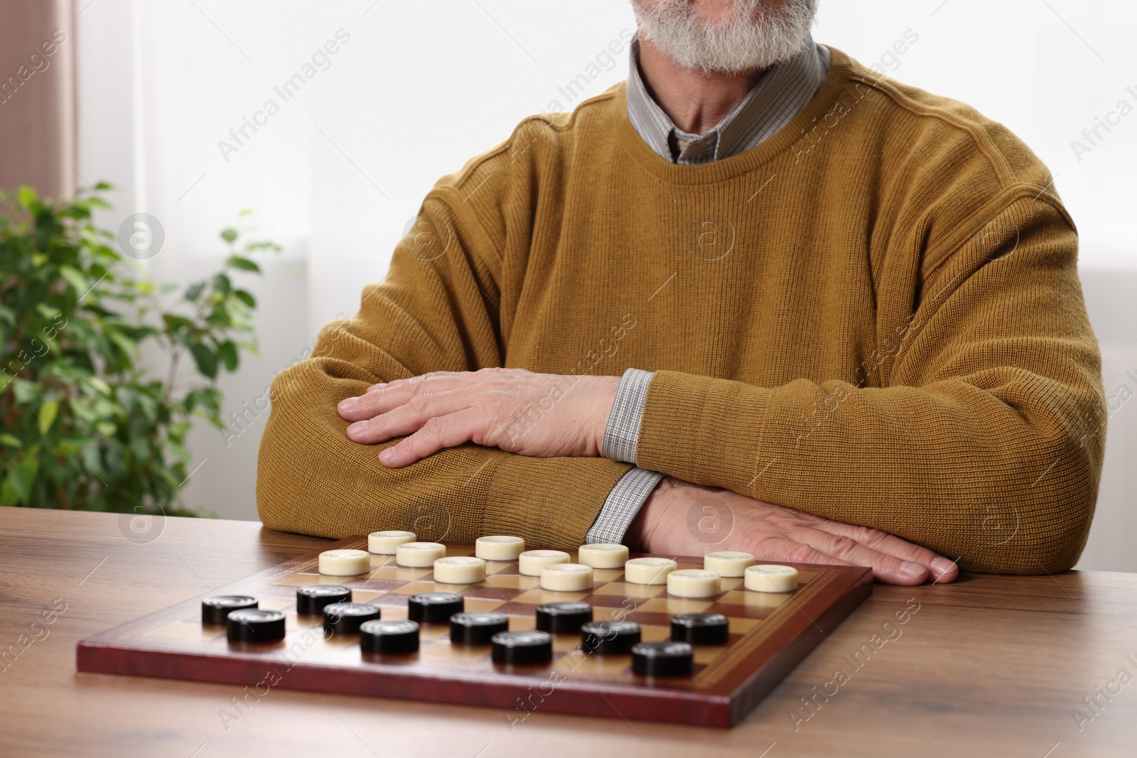 Photo of Playing checkers. Senior man thinking about next move at table in room, closeup