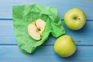 Photo of Whole and cut apples with beeswax food wrap on light blue wooden table, flat lay