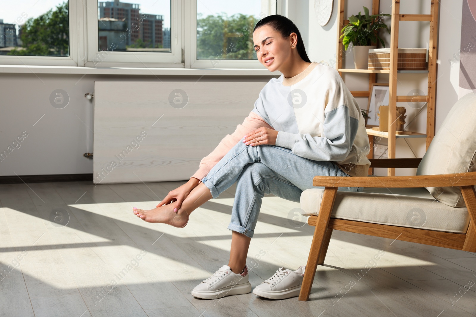 Photo of Young woman rubbing sore leg at home. Space for text