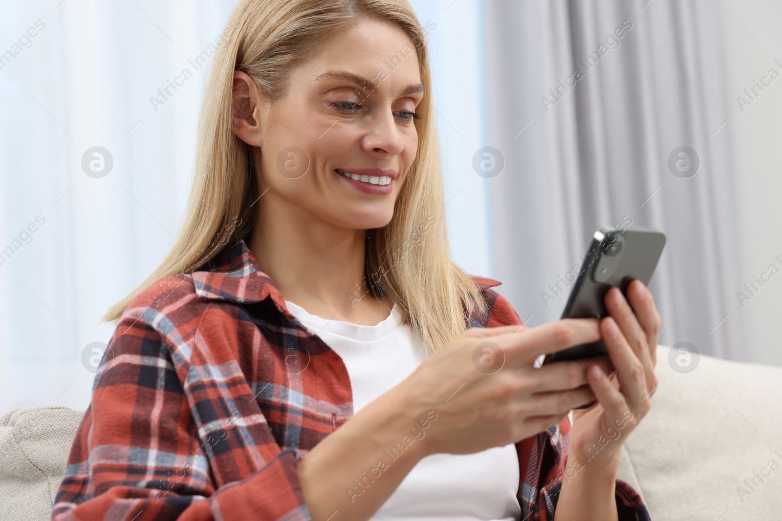 Photo of Happy woman sending message via smartphone at home