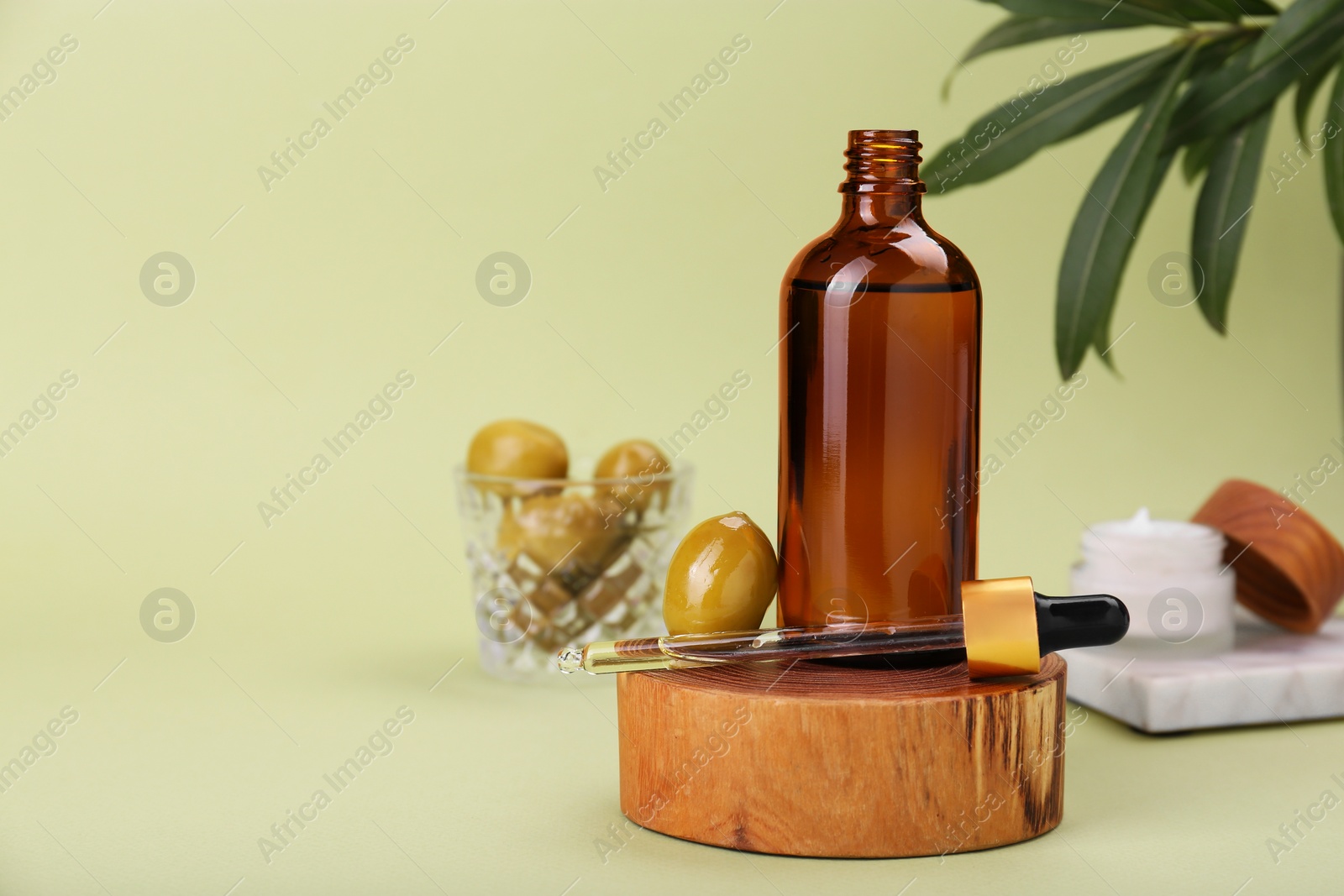 Photo of Glass bottle of serum and olives on green background, space for text