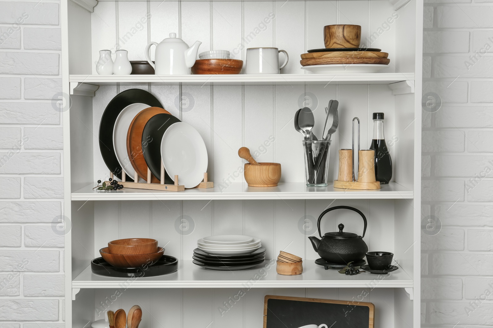 Photo of White shelving unit with set of dishware near brick wall