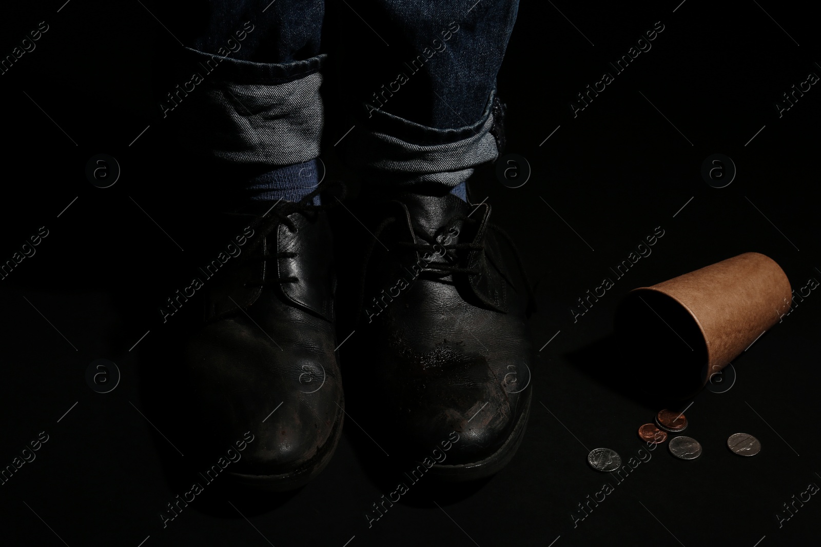 Photo of Poor man standing near cup with coins on dark background, closeup