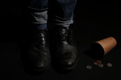 Poor man standing near cup with coins on dark background, closeup