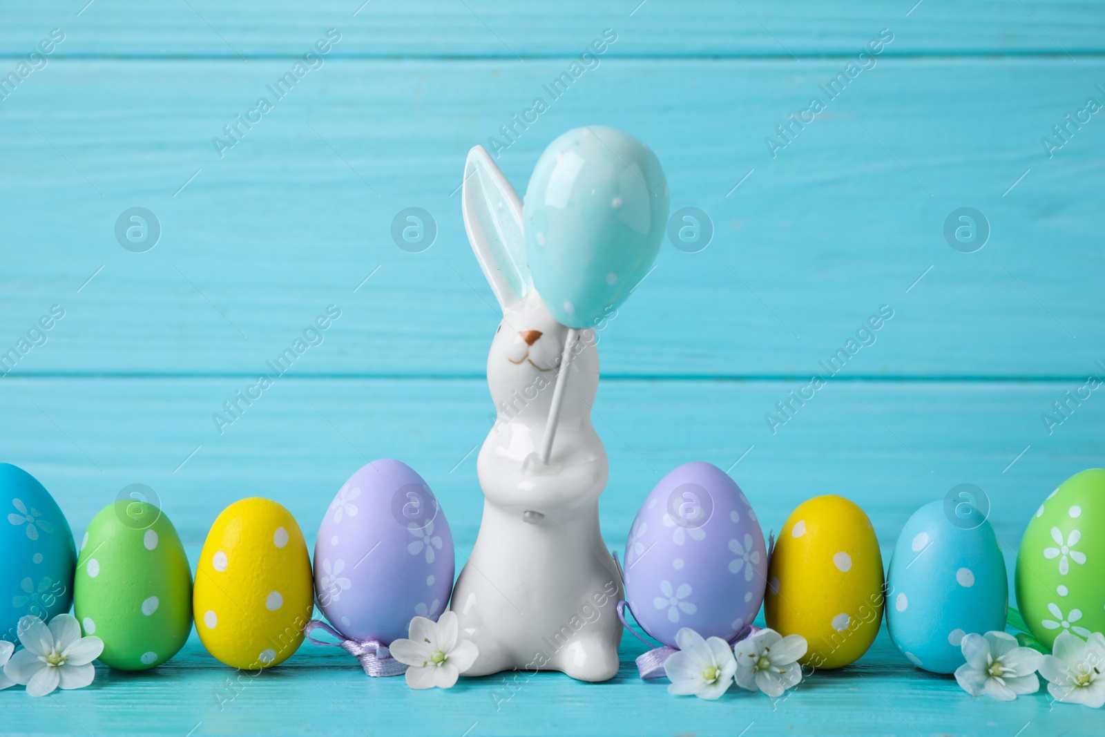 Photo of Easter bunny and painted eggs on light blue wooden background