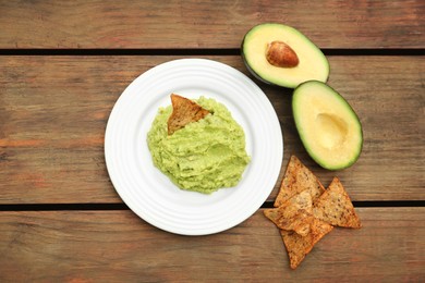 Photo of Delicious guacamole, avocado and nachos on wooden table, flat lay