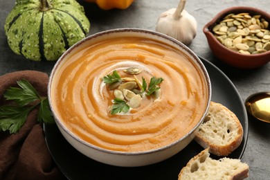 Photo of Delicious pumpkin soup in bowl served on grey textured table, closeup
