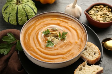 Delicious pumpkin soup in bowl served on grey textured table, closeup