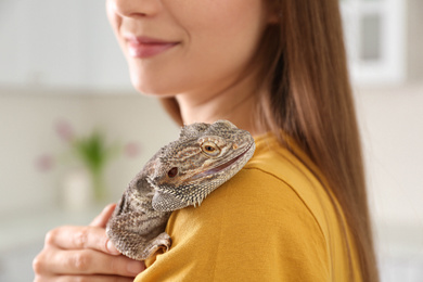 Photo of Woman holding bearded lizard indoors, closeup. Exotic pet