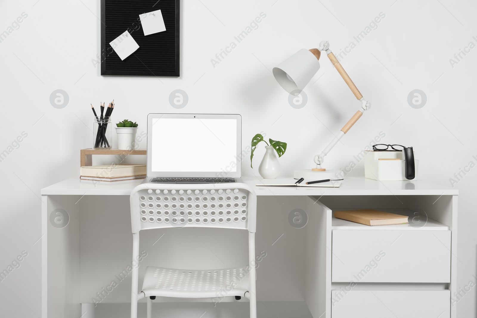 Photo of Cozy workspace with laptop, lamp and stationery on wooden desk at home