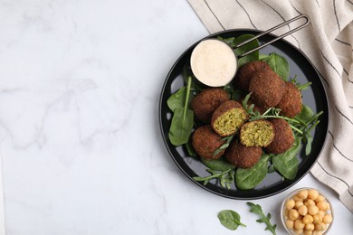 Photo of Delicious falafel balls, herbs, chickpeas and sauce on white marble table, top view. Space for text