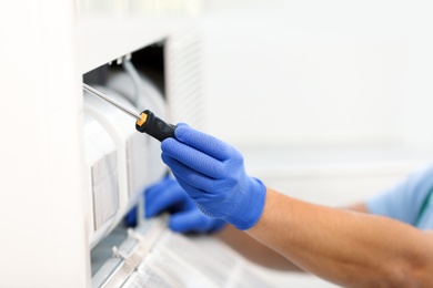Photo of Professional technician maintaining modern air conditioner indoors, closeup