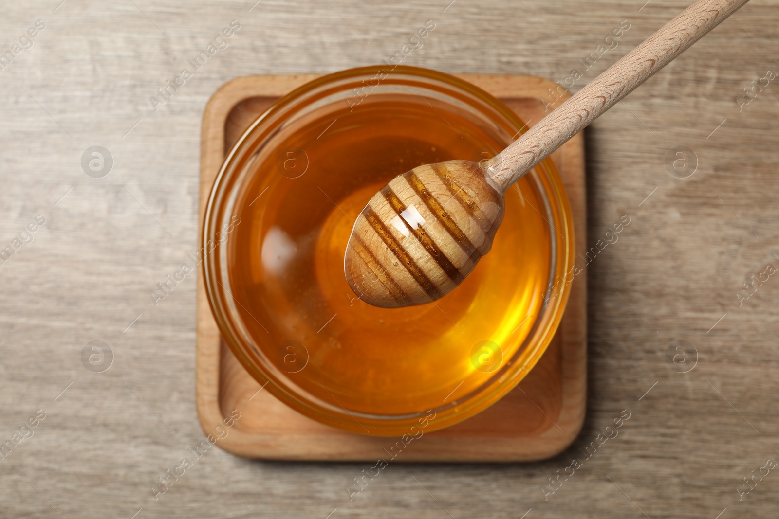 Photo of Dipper and glass bowl with honey on wooden table, top view