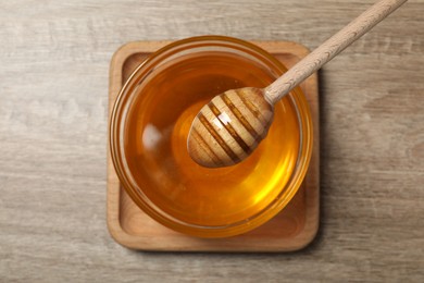 Photo of Dipper and glass bowl with honey on wooden table, top view