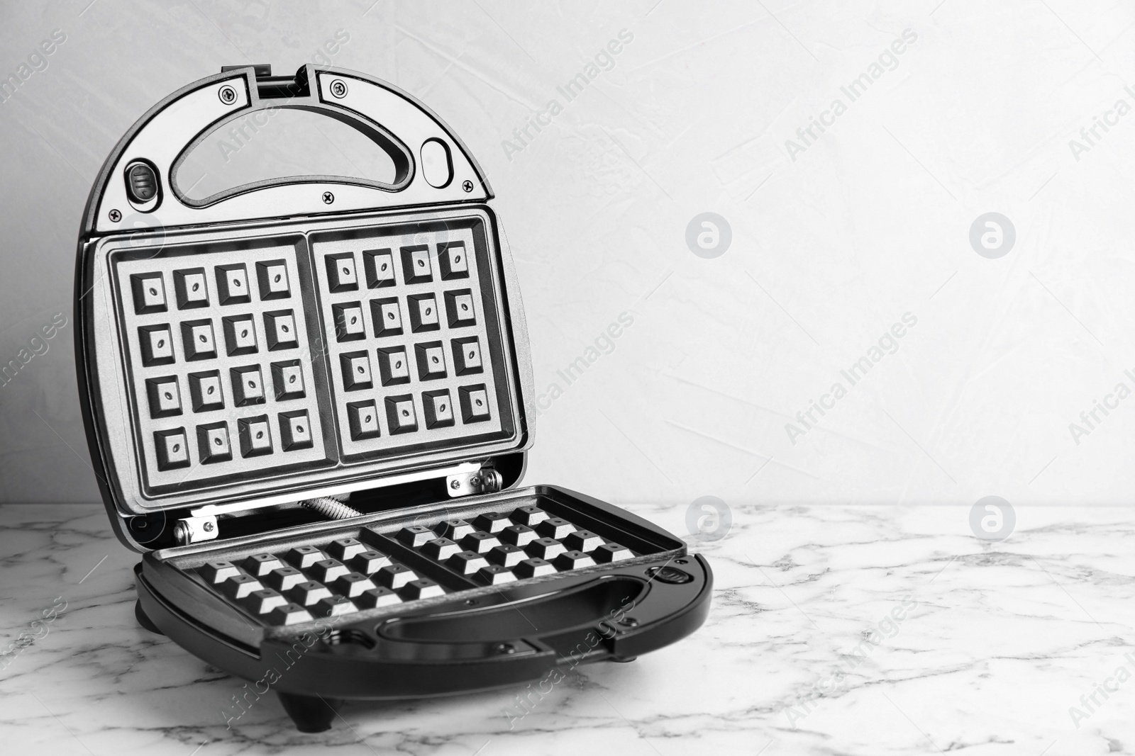 Photo of Modern waffle iron on white marble table. Space for text