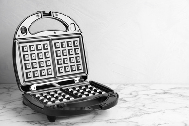 Photo of Modern waffle iron on white marble table. Space for text